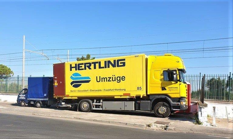 Gelber HERTLING LKW welcher Ladung umlädt in einen kleineren blauen Transporter